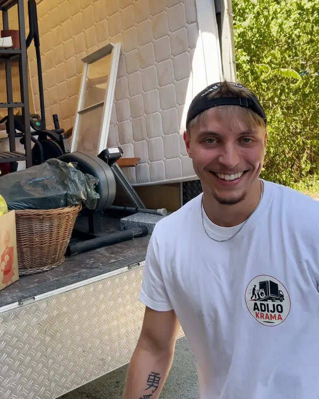 Nasmejan član ekipe Adijo Krama v majici z logotipom pred naloženim tovornjakom